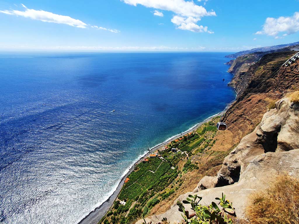 Tiefblick auf einen Küstenstreifen auf Madeira mit einer Seilbahn