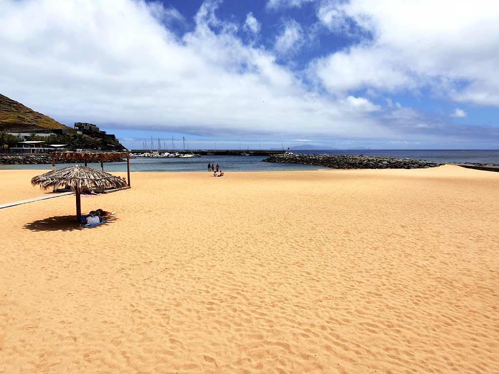 Madeira Strände: Heller Sandstrand mit Sonnenschirmen aus Stroh in Machico auf Madeira
