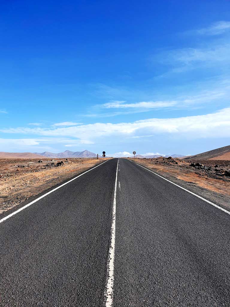 Mietwagen Tipps Fuerteventura Erfahrungen: Gerade, asphaltierte Strasse ohne Verkehr, die durch eine wundervolle Landschaft führt