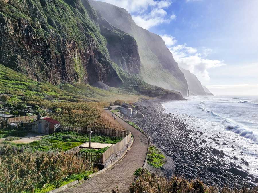 Achadas da Cruz Seilbahn: Die gut ausgebaute Promenade schlängelt sich zwischen den hohen Steilklippen und dem tosenden Atlantik hindurch. Vor diesem erstreckt sich ein steiniger Strand.