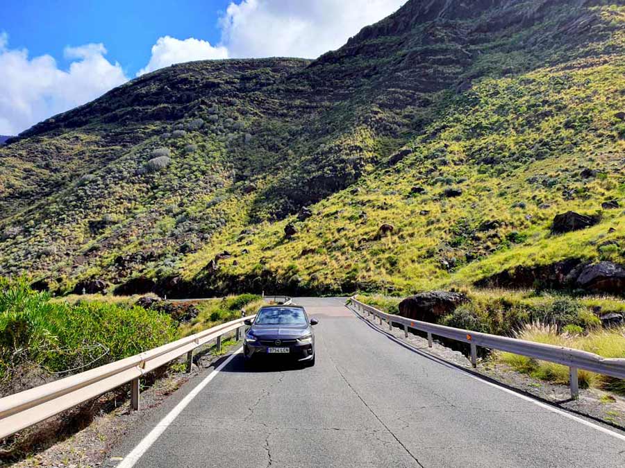 Mietwagen auf Gran Canaria im Winter am Fusse einer imposanten, grün leuchtenden Klippe