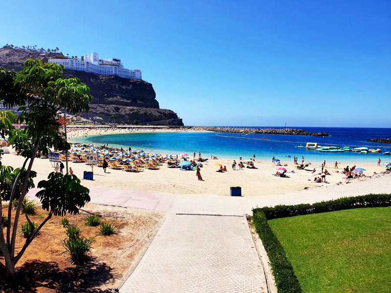 Türkis schimmerndes Wasser, heller Sand und Liegestühle am Strand Playa de Amadores auf Gran Canaria