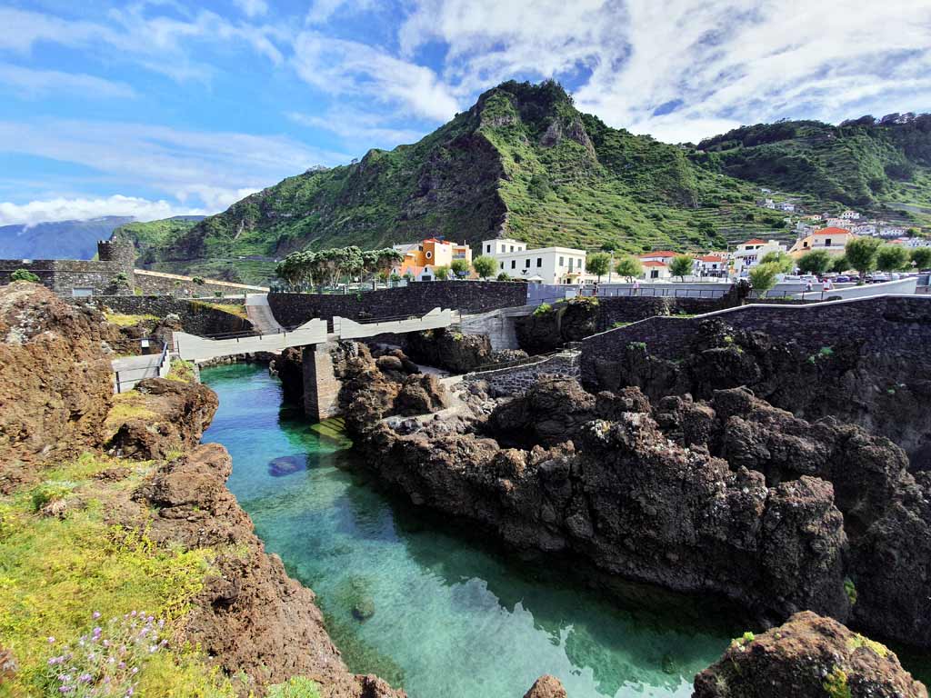 Porto Moniz Lavapools Madeira: Blick von den Piscinas Naturais Velhas auf die grünen Klippen hinter der Ortschaft Porto Moniz