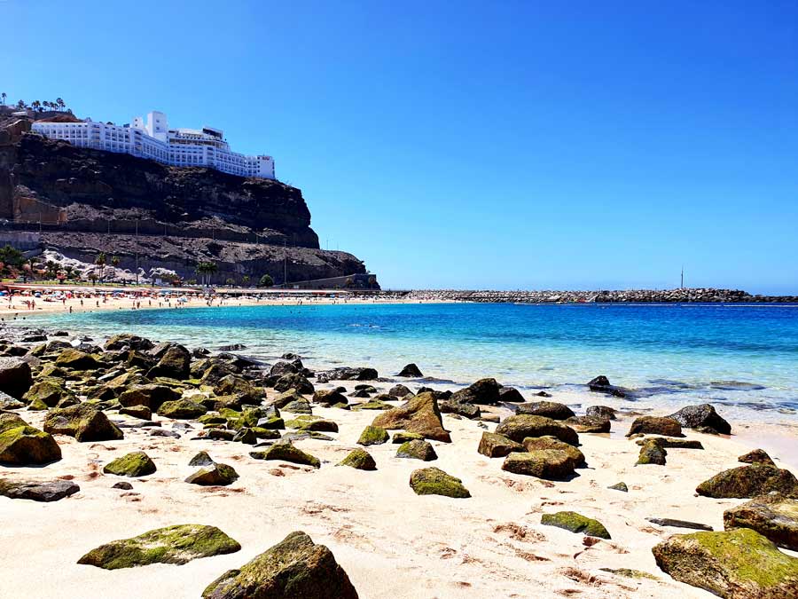 Gran Canaria wo übernachten: heller Sandstrand Playa de Amadores im Südwesten von Gran Canaria. Oben auf dem Felsen steht das Gran Canaria Hotel Riu Vistamar.