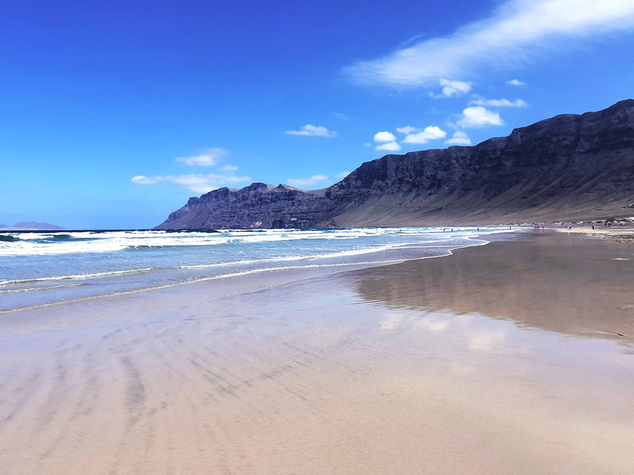 Lanzarote im Winter Erfahrungen Klima: Sonnenschein am beliebten Surferstrand Playa de Famara vor den imposanten Steilklippen